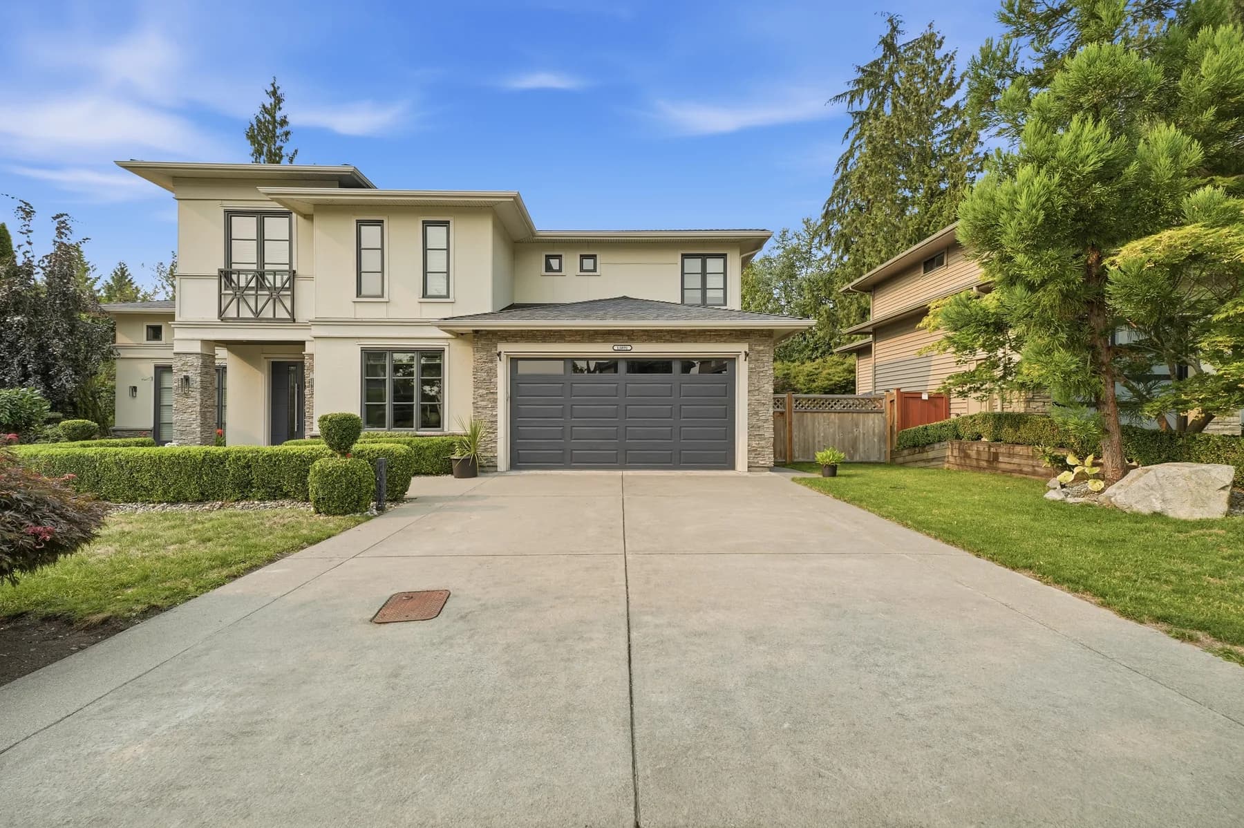 A large new build photographed vacant and staged: full front elevation, a double-height living space, a walnut island kitchen, and the folding glass wall standing open onto the covered deck.